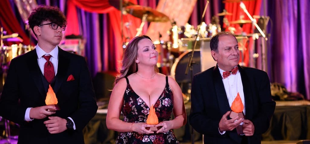 Three people on stage holding torch figurines.